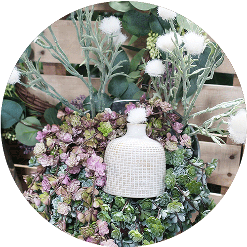 Artificial foliage of various types in a bucket, with a small white vase in the middle.